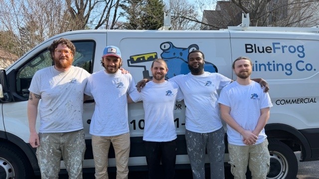 Five painters standing in front of a BlueFrog Painting Co. service van outdoors